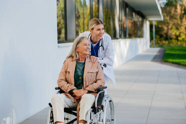 Junge Ärztin, die sich um eine ältere Frau in einem Rollstuhl kümmert. - HPIF10039