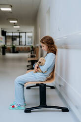 Kleines Mädchen, Patientin, sitzt allein mit ihrem Teddybär auf einem Krankenhausflur. - HPIF10051