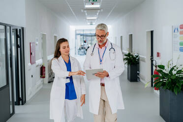 Älterer Arzt berät seinen jüngeren Kollegen bei einer Diskussion auf dem Krankenhausflur, Konzept der Gesundheitsversorgung. - HPIF10057