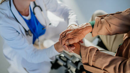 Nahaufnahme eines jungen Arztes, der die Hände einer Patientin im Rollstuhl hält und sie tröstet. - HPIF10084