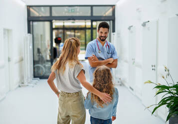 Ein junger Arzt spricht mit der Mutter eines kleinen Mädchens in einem Krankenhausflur. - HPIF10144