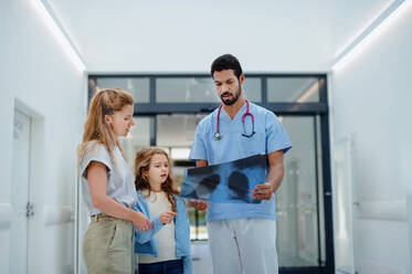 Ein junger Arzt spricht mit der Mutter eines kleinen Mädchens in einem Krankenhausflur. - HPIF10146