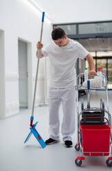 Young man with down syndrome working in hospital as cleaner. Concpet of integration people with disability into society. - HPIF10151