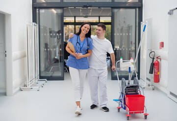 Young man with down syndrome working in hospital as cleaner, talking to nurse, having fun. Concpet of integration people with disability into society. - HPIF10173