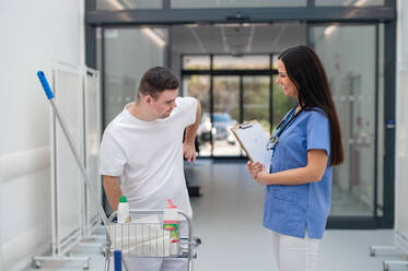 Young man with down syndrome working in hospital as cleaner, talking to nurse, having fun. Concpet of integration people with disability into society. - HPIF10174