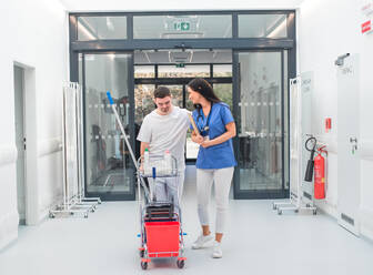 Young man with down syndrome working in hospital as cleaner, talking to nurse, having fun. Concpet of integration people with disability into society. - HPIF10180