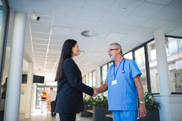 Junge Geschäftsfrau schüttelt einem älteren Arzt in einem Krankenhauszimmer die Hand. - HPIF10202