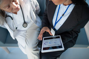 Hohe Winkelansicht einer Geschäftsfrau, die einem Arzt im Krankenhaus ein Diagramm auf einem digitalen Tablet zeigt. - HPIF10214