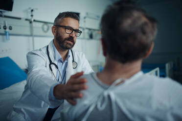 Mature doctor consoling and explaining diagnosis to his patient in hospital room. - HPIF10243