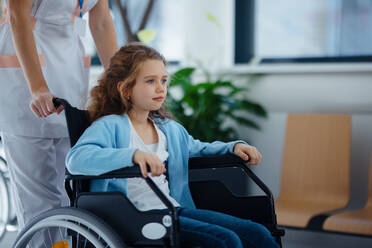 Krankenschwester schiebt kleines Mädchen im Rollstuhl auf einem Krankenhausflur. - HPIF10259