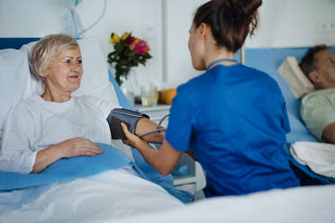 Junge Krankenschwester misst Blutdruck bei einem älteren Patienten. - HPIF10268