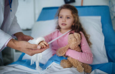 Ein Arzt untersucht ein kleines Mädchen mit gebrochenem Arm. - HPIF10279