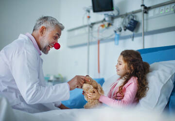 Glücklicher Arzt mit roter Clownsnase, der sich um ein kleines Mädchen kümmert und mit ihm spielt. - HPIF10280