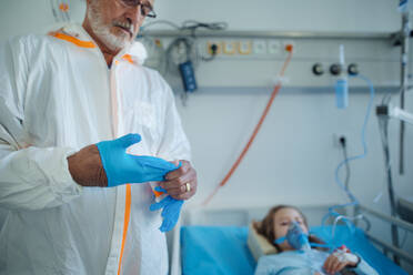 Doctor in protective coverall putting off surgical gloves after examination of little girl. - HPIF10291