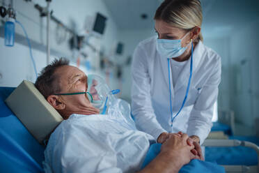 Junge Ärztin im Gespräch mit älterem Patienten mit Sauerstoffmaske in einem Krankenhauszimmer. - HPIF10310