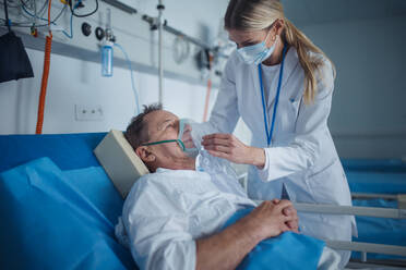 Junge Ärztin, die einem älteren Patienten im Krankenhauszimmer eine Sauerstoffmaske aufsetzt. - HPIF10311