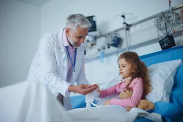 Ein Arzt untersucht ein kleines Mädchen mit gebrochenem Arm. - HPIF10343