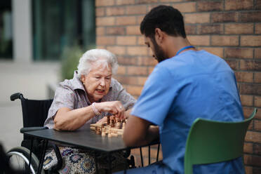 Betreuer spielt mit seinem Klienten draußen in einem Café Schach. - HPIF10386