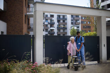 Caregiver walking with senior woman client in front of a nurishing home. - HPIF10414