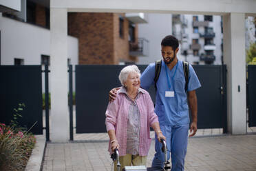 Caregiver walking with senior woman client in front of a nurishing home. - HPIF10415