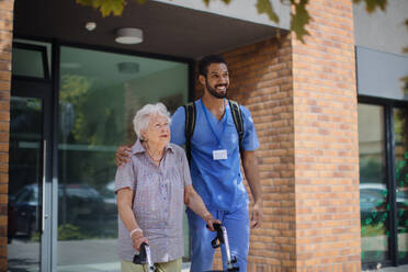 Caregiver walking with senior woman client in front of a nurishing home. - HPIF10426