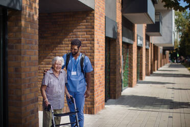 Caregiver walking with senior woman client in front of a nurishing home. - HPIF10427