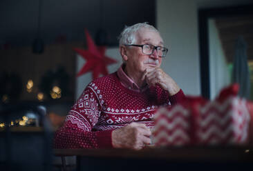 Unglücklicher älterer Mann, der allein sitzt und auf seine Familie wartet, während des Weihnachtsabends. Konzept der Einsamkeit der Senioren. - HPIF10489