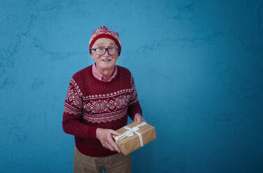 Portrait of happy senior man holding gift, in front of blue background. - HPIF10498