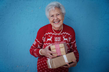 Porträt einer glücklichen älteren Frau, die ein Geschenk hält, vor einem blauen Hintergrund. - HPIF10502