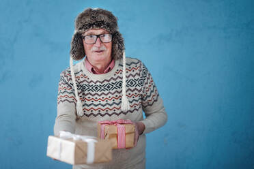 Portrait of happy, excited senior man in warm Chrstimas cap holding gifts. - HPIF10518