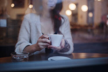 Nahaufnahme einer Frau mit einer Tasse Kaffee in der Hand, die in einem Café sitzt. - HPIF10538