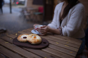 Nahaufnahme einer Frau mit einer Tasse Kaffee und frischem Gebäck, die in einem Café sitzt. - HPIF10539