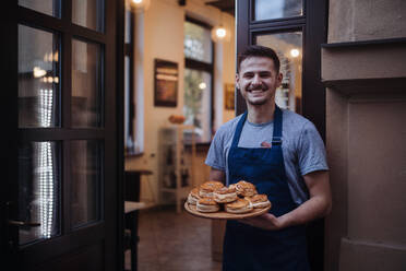 Man with apron holding fresh pastries, standing at the door. - HPIF10541