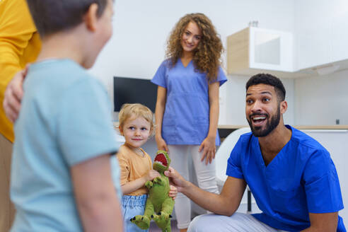 Junger multirassischer Zahnarzt spielt mit Kindern in seinem Büro in einer Zahnklinik. - HPIF10547