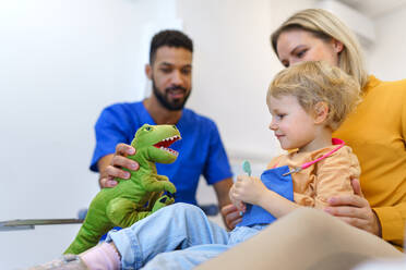 Junger multirassischer Zahnarzt spielt mit Kindern in seinem Büro in einer Zahnklinik. - HPIF10553