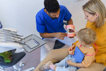 Junger multirassischer Zahnarzt zeigt einem kleinen Mädchen, wie man Zähne putzt. - HPIF10555