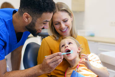 Ein kleines Mädchen sitzt mit ihrer Mutter auf dem Zahnarztstuhl während einer zahnärztlichen Untersuchung. - HPIF10562