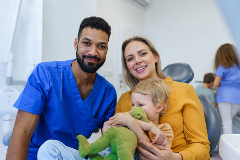 Porträt eines multirassischen Zahnarztes und einer jungen Mutter mit kleinem Kind auf einem Zahnarztstuhl. - HPIF10575