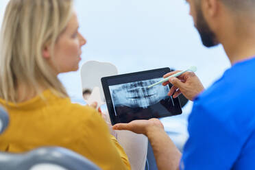 Rückansicht eines Zahnarztes, der dem Patienten eine Röntgenaufnahme auf einem digitalen Tablet zeigt. - HPIF10582