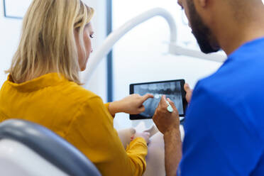 Rear view of dentist showing x-ray scan at digital tablet to patient. - HPIF10584