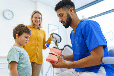 Junger Zahnarzt zeigt kleinen Jungen, wie man die Zähne reinigt, Konzept der Mundhygiene für Kinder, Prävention und Zahngesundheit. - HPIF10591