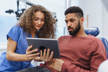 Young woman dentist doing preventive examination to multiracial man, showing him x-ray image in a digital tablet. - HPIF10607