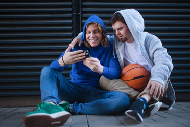 Man with down syndrome resting during basketball playing outdoor with his friend. Concept of friendship and integration people with disability into a society. - HPIF10629