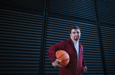 Porträt eines jungen Mannes mit Down-Syndrom, der einen Basketball hält. - HPIF10634