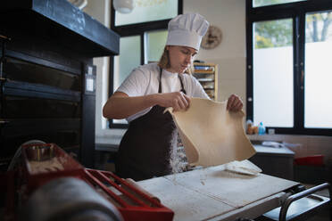 Young baker with chef cap preparing pastries in a bakery. - HPIF10640