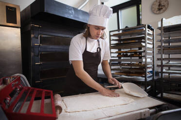 Junger Bäcker mit Kochmütze bei der Zubereitung von Gebäck in einer Bäckerei. - HPIF10642