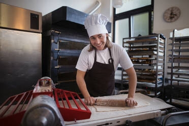 Junger Bäcker mit Kochmütze bei der Zubereitung von Gebäck in einer Bäckerei. - HPIF10644