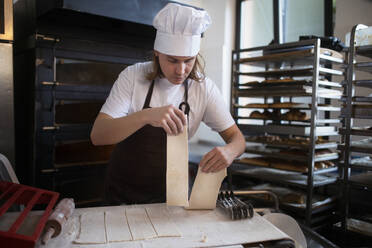 Junger Bäcker mit Kochmütze bei der Zubereitung von Gebäck in einer Bäckerei. - HPIF10647