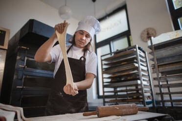 Junger Bäcker mit Kochmütze bei der Zubereitung von Gebäck in einer Bäckerei. - HPIF10651