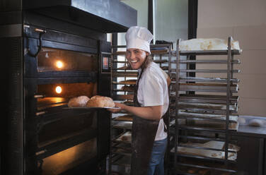 Junger Bäcker mit Kochmütze bei der Zubereitung von Gebäck in einer Bäckerei. - HPIF10655